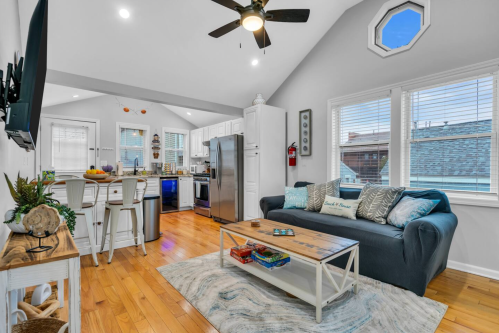Bright, modern living room with a blue sofa, coffee table, and open kitchen featuring white cabinets and hardwood floors.
