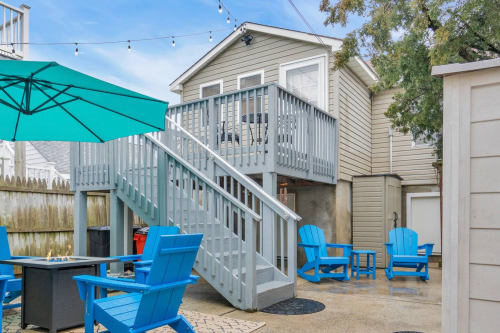 A cozy outdoor space featuring blue chairs, a patio table, and a two-story house with a deck and string lights.