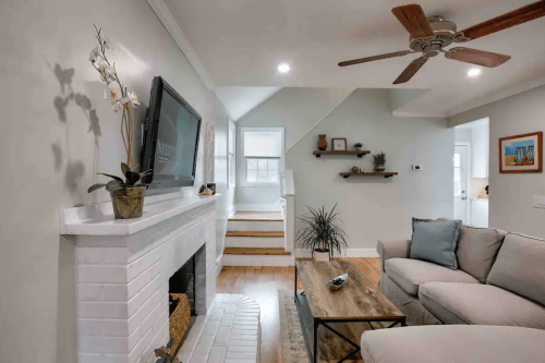 Cozy living room with a white brick fireplace, modern furniture, and a staircase leading to an upper level.