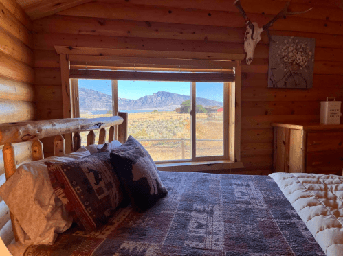 Cozy log cabin bedroom with a bed, patterned blanket, and a large window showcasing a mountain view.
