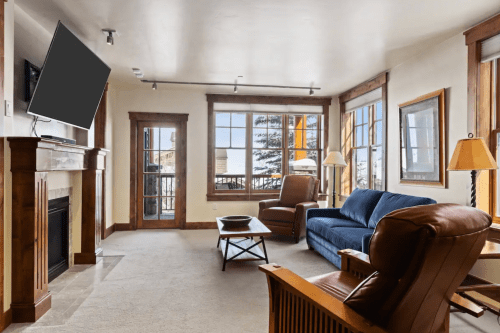 Cozy living room with a blue sofa, armchairs, fireplace, and large windows overlooking a snowy landscape.