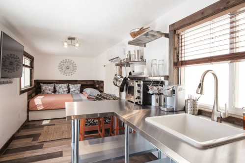A cozy studio with a kitchen area, dining table, and a bed in the background, featuring modern decor and natural light.