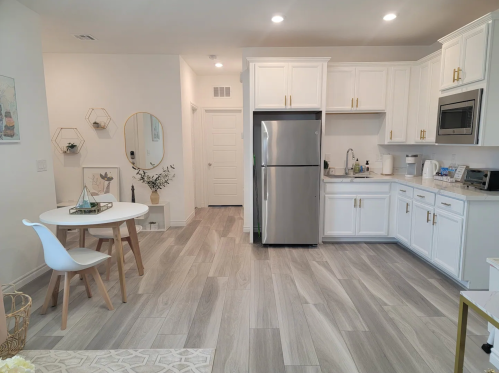 Modern kitchen and dining area with white cabinets, stainless steel appliances, and a round table with chairs.