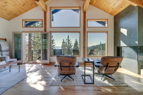 Cozy living room with large windows, wooden ceiling, and modern furniture, overlooking a scenic forest view.