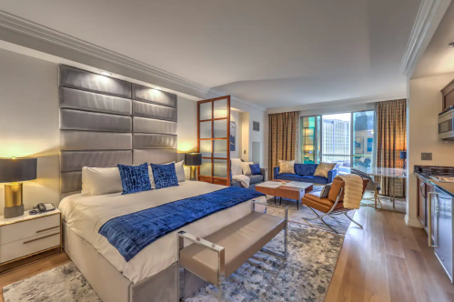 A modern hotel room featuring a king bed, seating area, large windows, and stylish decor.