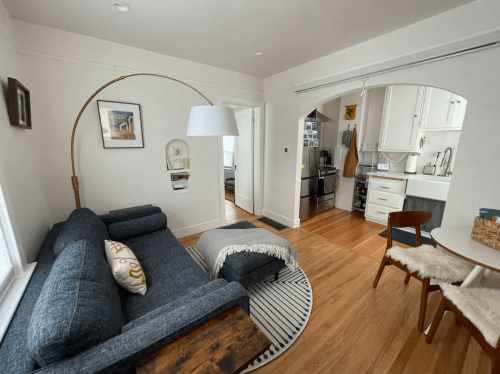 Cozy living space featuring a gray sofa, a floor lamp, and a dining area with a round table in a bright, modern apartment.