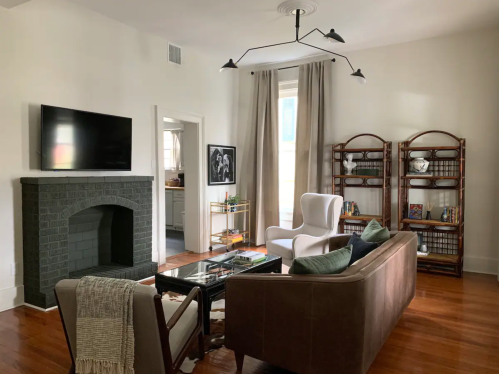 Cozy living room with a TV, fireplace, bookshelves, and comfortable seating, featuring warm wood floors and natural light.