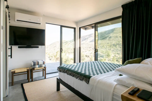 A modern bedroom with a bed, TV, and large windows overlooking a mountainous landscape.
