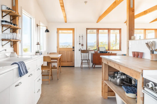 Bright, modern kitchen with wooden beams, a dining area, and large windows showcasing a scenic view.