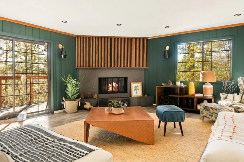 Cozy living room with a fireplace, large windows, green walls, and modern furniture, featuring a warm, inviting atmosphere.