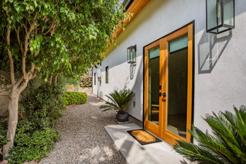 A modern entrance with wooden doors, surrounded by greenery and gravel pathways, leading to a bright, inviting home.