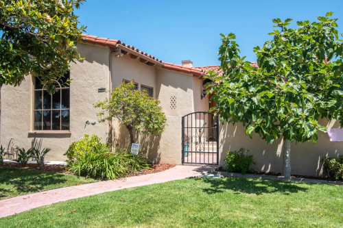 A charming house with a gated entrance, surrounded by greenery and a clear blue sky.