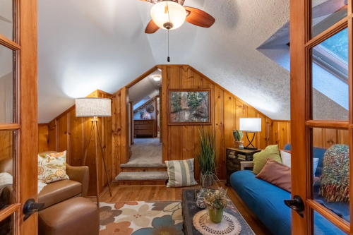 Cozy attic living space with wooden walls, a blue sofa, armchair, and decorative lamps, featuring a warm, inviting atmosphere.