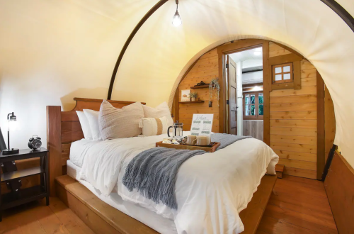 Cozy, circular bedroom with a wooden bed, soft bedding, and a tray with breakfast items on a rustic wooden floor.