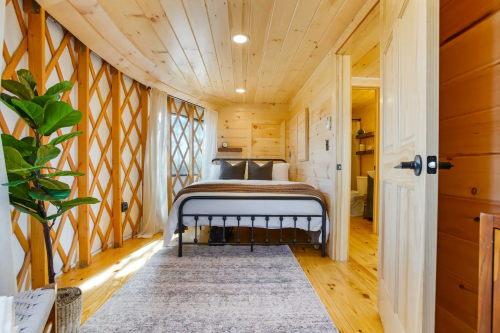 Cozy wooden bedroom with a bed, natural light, and a plant, featuring a warm, rustic design.