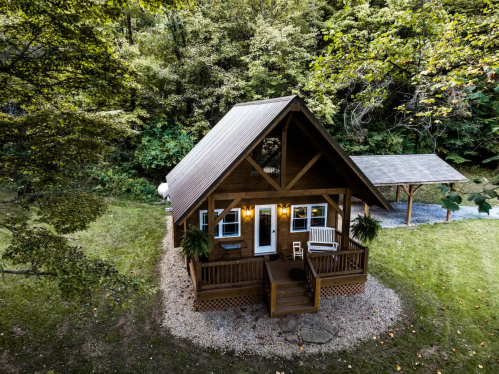 A cozy wooden cabin surrounded by trees, featuring a porch and a gravel path, set in a serene outdoor environment.