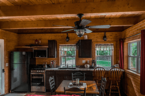 Cozy kitchen with wooden beams, dark cabinets, a dining table, and large windows letting in natural light.