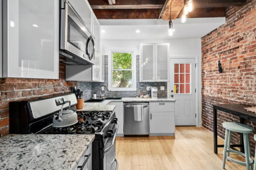Modern kitchen with stainless steel appliances, granite countertops, exposed brick walls, and wooden beams.