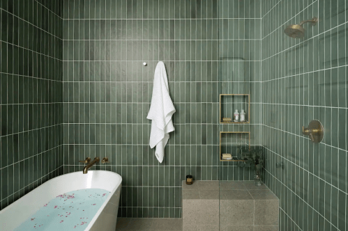 A modern bathroom with green tiled walls, a white bathtub filled with water, and a towel hanging on the wall.