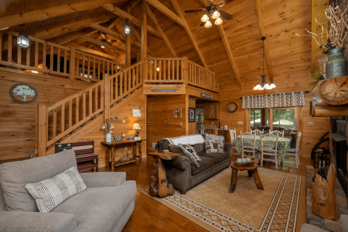 Cozy wooden cabin interior with a living area, staircase, and rustic decor, featuring a sofa and wooden furniture.