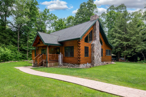 A charming log cabin surrounded by lush greenery, featuring a stone chimney and a winding pathway.