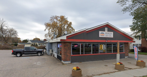 A burger restaurant with a red and gray exterior, featuring a sign and outdoor seating, set in a suburban area.