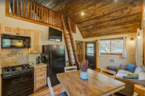 Cozy cabin interior featuring a kitchen, dining area, and lofted sleeping space with wooden accents and natural light.