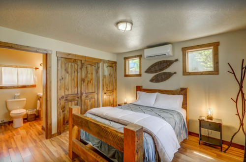 Cozy bedroom with a wooden bed, natural decor, and an adjoining bathroom, featuring warm lighting and rustic elements.