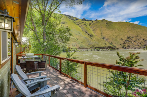 A scenic deck overlooking a river, surrounded by lush green hills and trees under a clear blue sky.