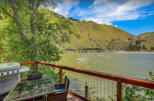 Scenic view from a deck overlooking a river, surrounded by green hills and trees under a blue sky.