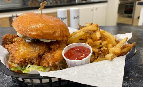A crispy fried chicken sandwich with lettuce and sauce, served with a side of golden fries and ketchup in a basket.