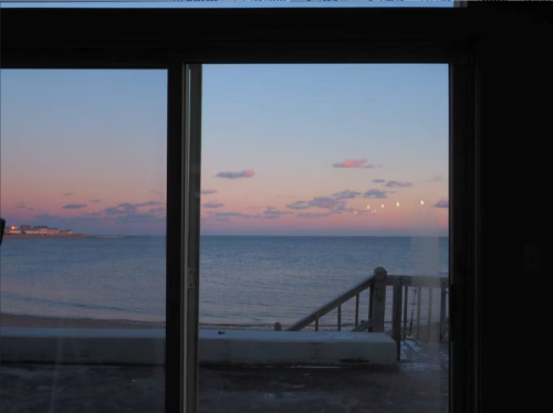 A serene view of the ocean at sunset, with soft pink and blue hues visible through a large glass window.