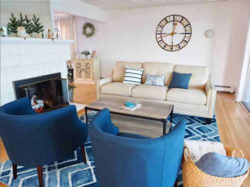 Cozy living room with a beige sofa, blue chairs, a wooden coffee table, and a decorative fireplace.