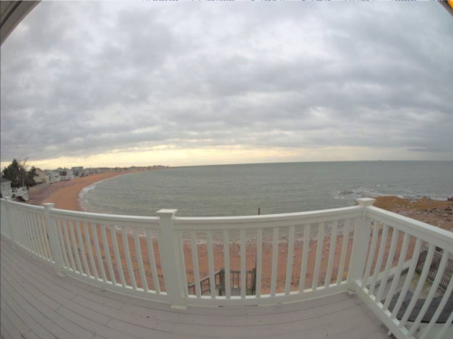 View from a balcony overlooking a sandy beach and calm sea under a cloudy sky.