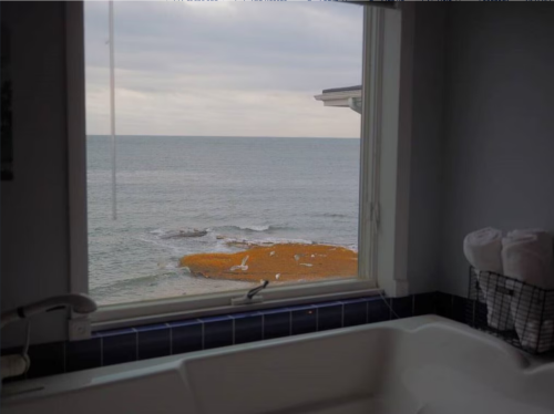 View from a bathroom window overlooking a calm sea and rocky shore, with towels neatly arranged nearby.