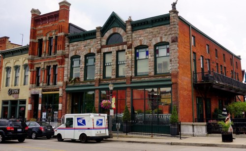 Historic brick buildings with stone accents, featuring a USPS delivery truck parked in front.