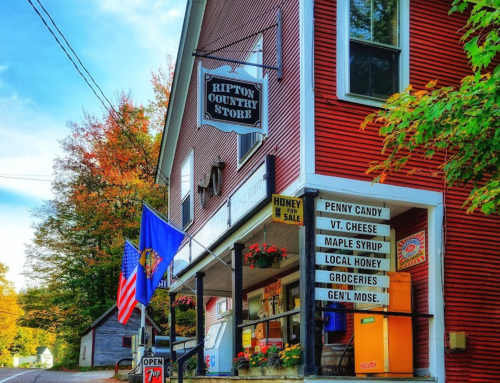 A charming country store with a red exterior, signs for local goods, and autumn foliage in the background.