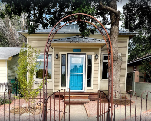 A charming house with a blue door, surrounded by greenery and a decorative archway at the entrance.