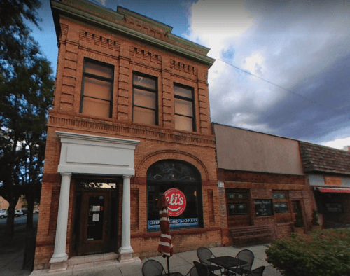 Historic brick building with large windows, featuring a sign for "Eli's" and outdoor seating in front.
