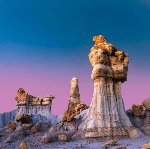 A surreal landscape of towering rock formations under a twilight sky with stars, showcasing vibrant colors and textures.
