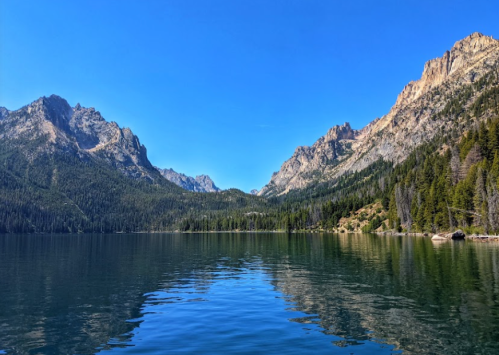 A serene lake surrounded by mountains and lush greenery under a clear blue sky.