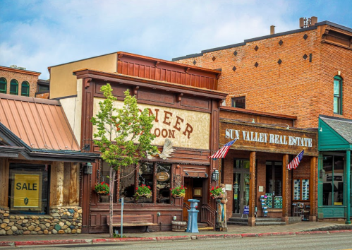 Historic buildings with wooden facades and American flags in a quaint town, featuring shops and a saloon.