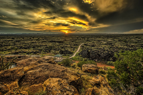 A dramatic sunset over a rocky landscape, with winding paths and scattered vegetation under a colorful sky.