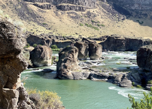 A serene river flows through rocky terrain, surrounded by dry hills and lush greenery.