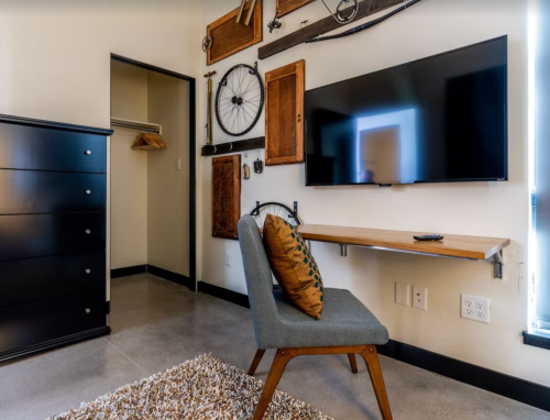 A modern room featuring a wall with decor, a TV, a wooden desk, a chair, and a dresser.