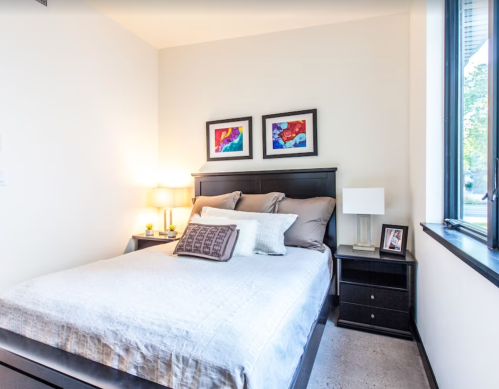 Cozy bedroom featuring a bed with decorative pillows, bedside lamp, and framed artwork on the wall.