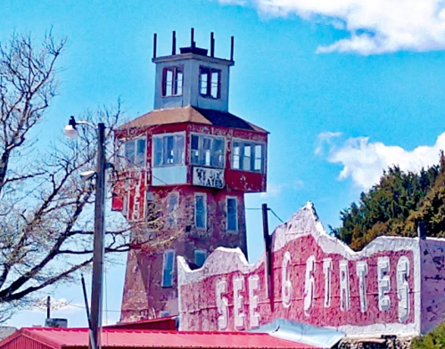 A tall, weathered tower with a red roof and a sign reading "See 16 States" against a blue sky with scattered clouds.