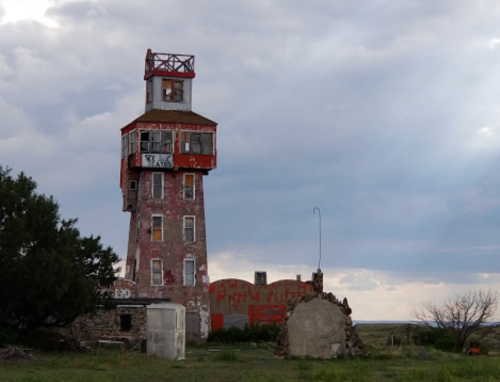 A tall, weathered tower with graffiti, surrounded by sparse vegetation and a cloudy sky.