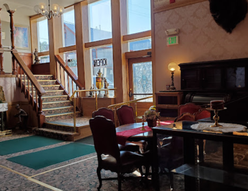 Elegant lobby with a staircase, vintage furniture, and large windows letting in natural light.