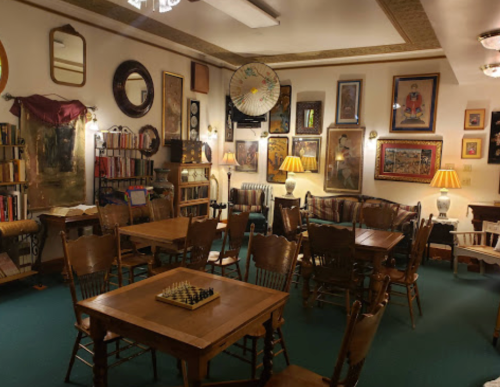 Cozy room with wooden tables, chairs, a chessboard, and walls adorned with various framed artworks and mirrors.